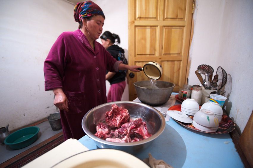 Женщина в домашней одежде готовит мясо в сельской кухне Казахстана