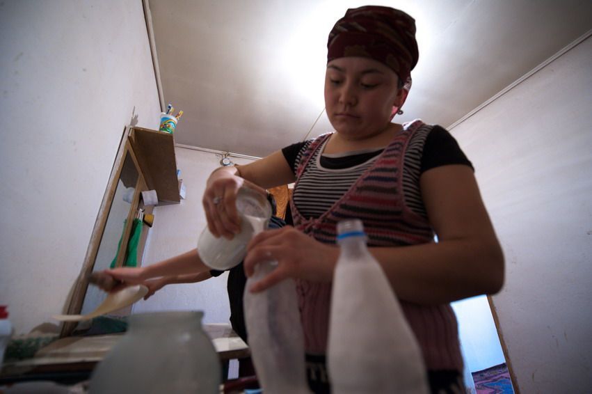 Молодая женщина переливает кефир или айран в бутылки на домашней кухне Казахстана