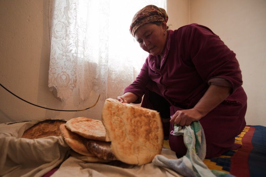 Женщина в сельском доме складывает свежеиспечённые лепёшки на ткань у окна в Казахстане